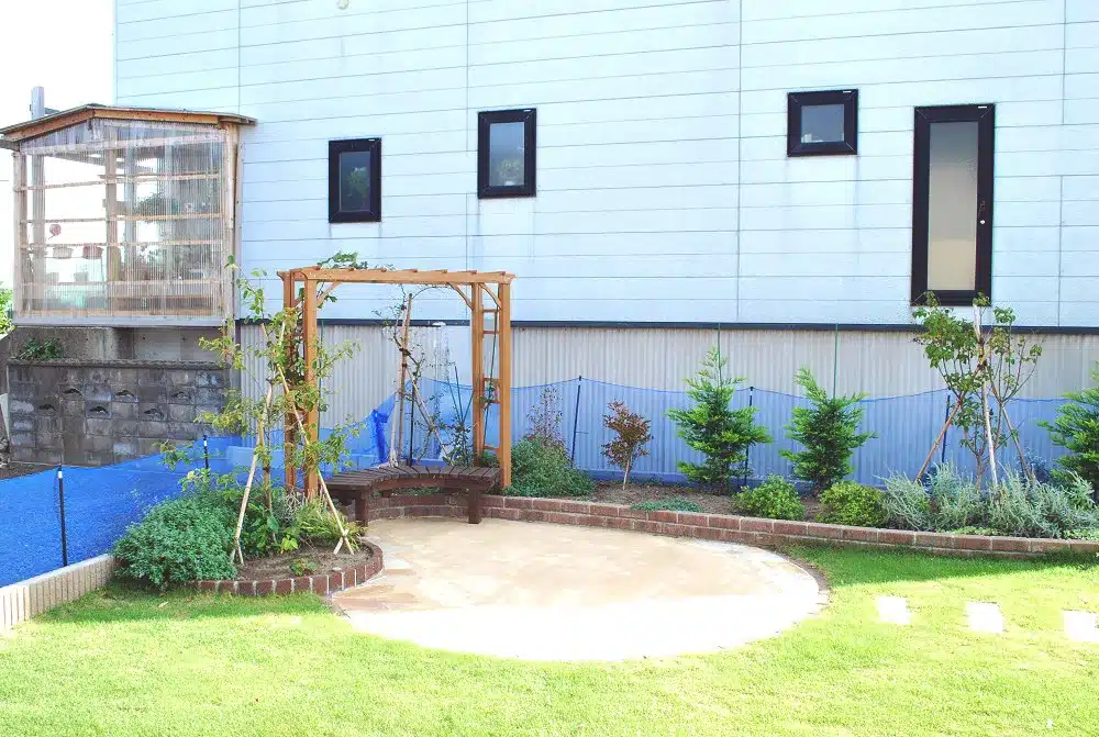 田の住宅裏庭に設置された木製パーゴラとベンチ、周囲の植栽と芝生の庭。