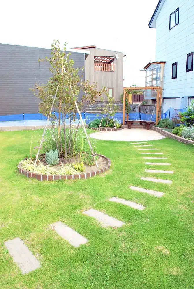 秋田の庭に敷かれた枕木風の飛び石の園路と、中央の植栽、奥のパーゴラ。