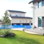 秋田の住宅の掃き出し窓に続く広いテラスと、手前の芝生、奥の庭の様子。