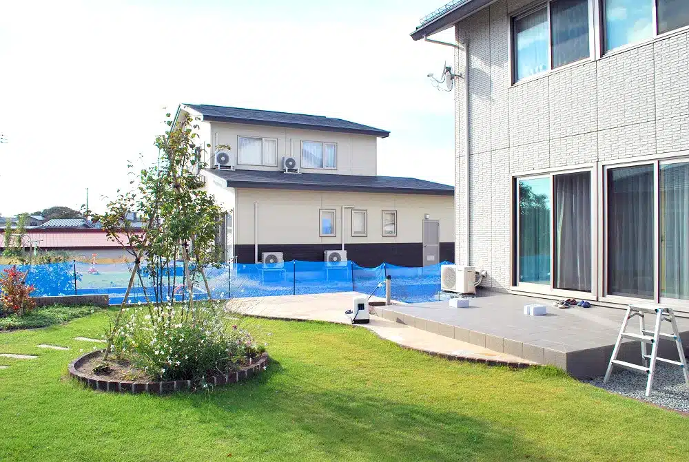 秋田の住宅の掃き出し窓に続く広いテラスと、手前の芝生、奥の庭の様子。