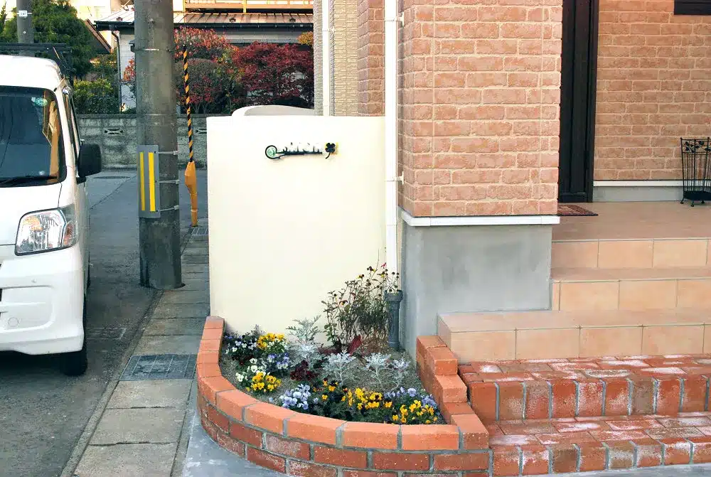 秋田市S様邸の玄関前にある白い門柱とレンガの低い花壇、そして色とりどりの花々。