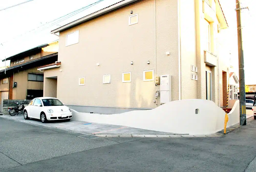 秋田市S様邸の敷地全体を覆う、緩やかな曲線を描く白い塗り壁のクローズド外構と駐車スペース。