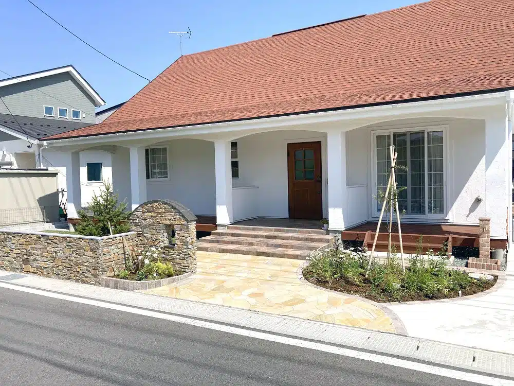 南欧風住宅の前面全景。天然石の門柱と乱張りアプローチ、適度な高さの塀、そしてガーデニングスペース。