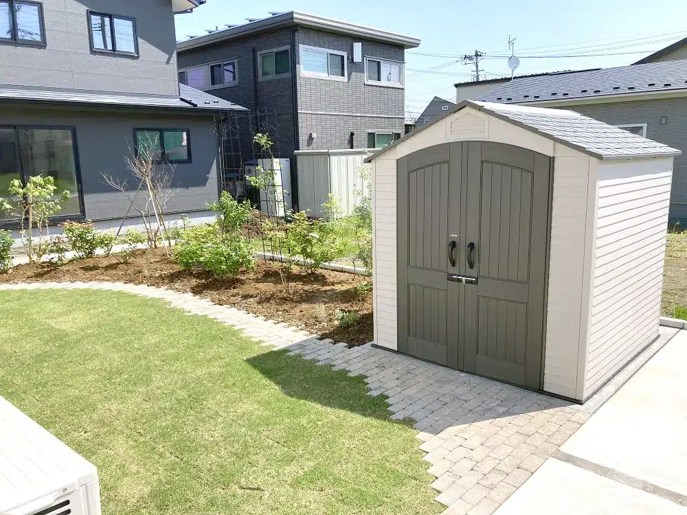 広大な芝生が広がる庭の奥に佇む、アーチ型の扉が特徴的なデザイン物置。