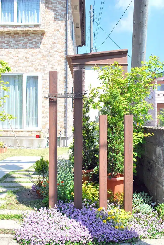 秋田市W様邸の玄関アプローチにある木調の門柱と、足元に広がる美しい花々の植栽。