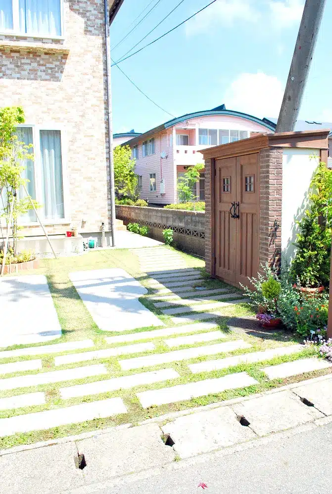 秋田市W様邸の敷地の側面を奥へと続く、枕木風の飛び石の園路と住宅外壁。