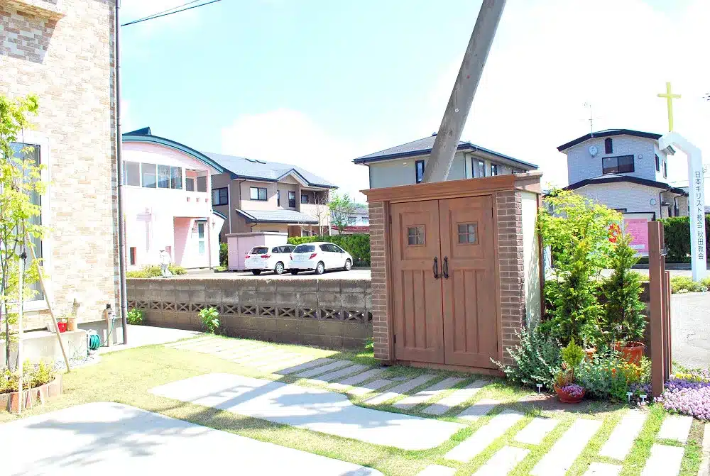 秋田市W様邸の、デザイン物置と枕木風のアプローチ、広がる開放的な庭の風景。