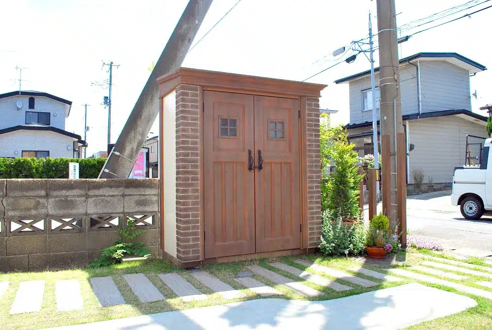 秋田市W様邸の、レンガ調のデザインが施されたカントリー風の物置と枕木風の飛び石のアプローチ。