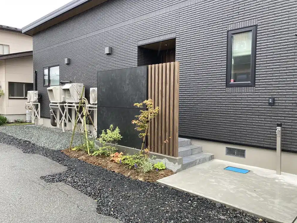 秋田の住宅玄関横に設置された、黒いパネルと木目調の角柱を組み合わせたモダンな目隠しフェンス。