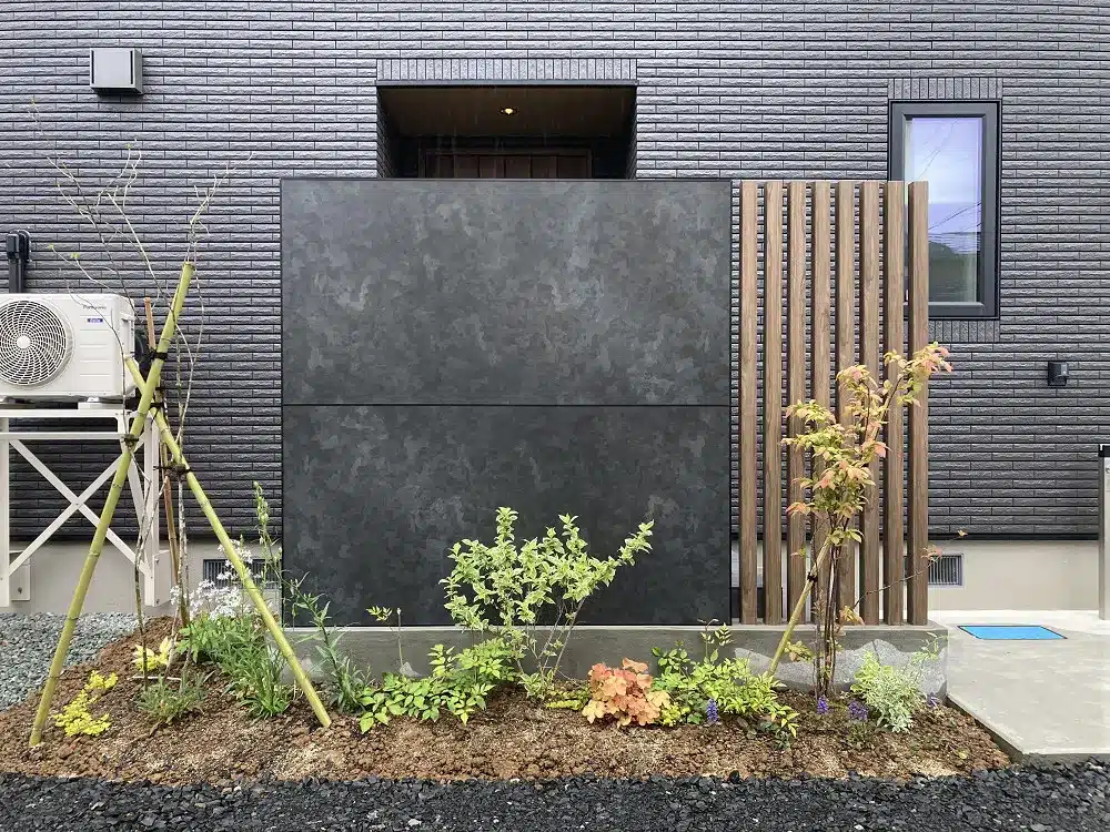 秋田の住宅玄関前の、黒いエバーアートボードと植栽を配したシックな目隠しデザイン。