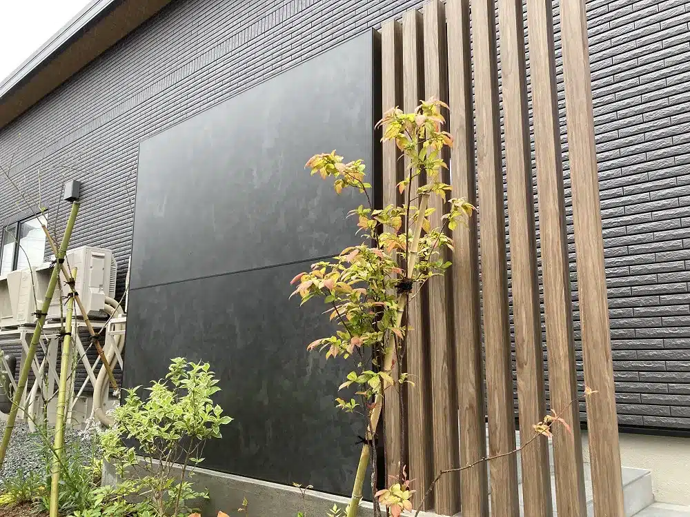 秋田の住宅玄関目隠しのクローズアップ。黒いパネルと木目調の角柱、そして手前の植栽の配置。