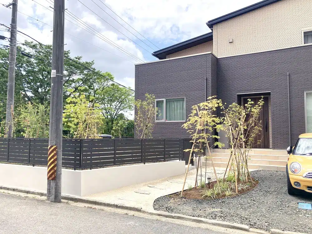 道路側から見た秋田市K様邸の外構全景。弾性塗装された擁壁とアルミフェンスが印象的なリフォーム事例。