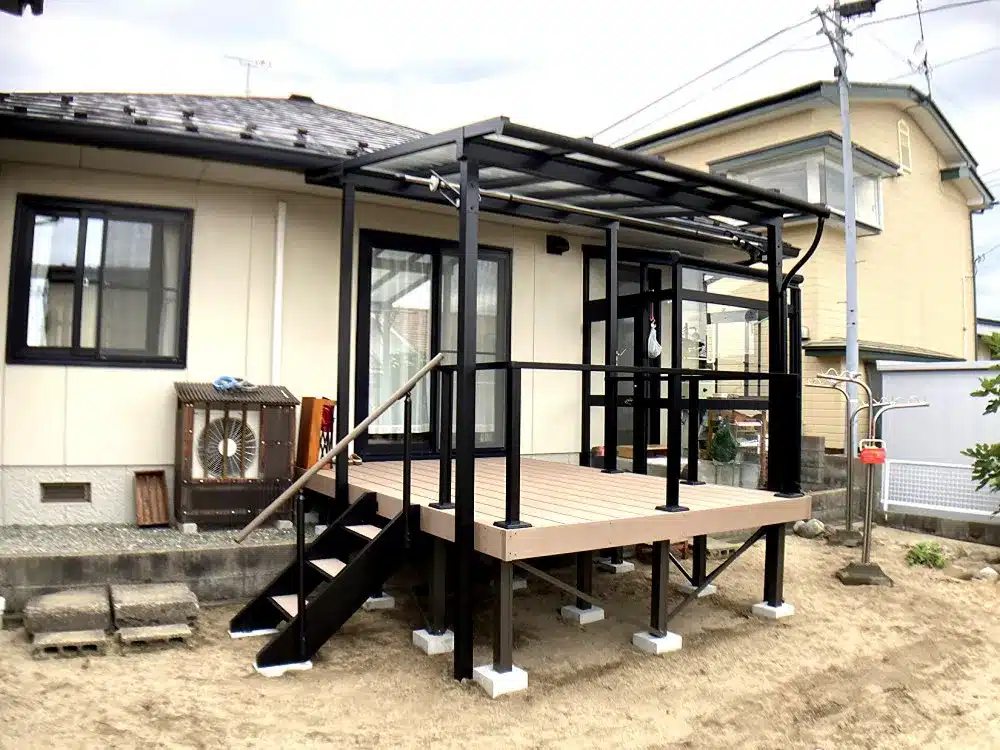 秋田市T様邸の住宅脇に設置された、黒いフレームのテラス屋根付き樹脂デッキと階段。