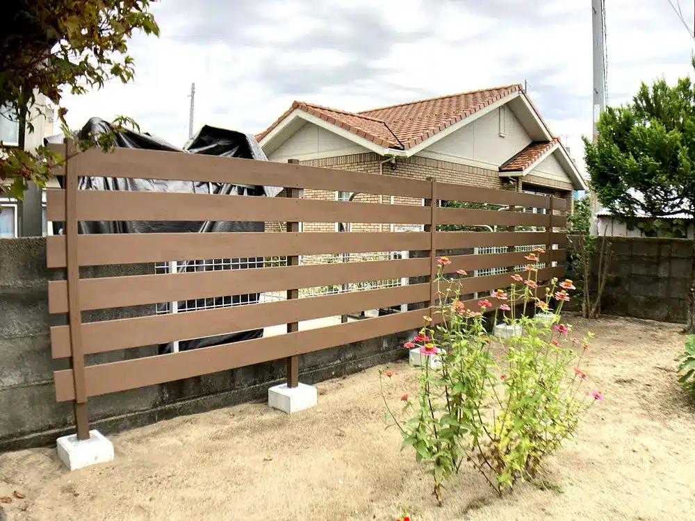 秋田市T様邸の庭の境界に設置された、木目調の樹脂製横板目隠しフェンスと花壇。