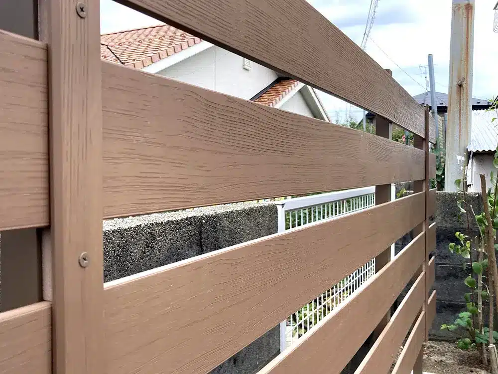 木目調の樹脂フェンスの表面テクスチャと、隣接する構造物のクローズアップ。